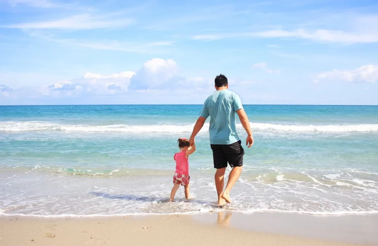 Luxury south african safari- father and daughter hold hands and walking in ocean water on a beach