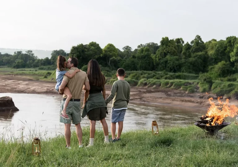 Typical day- a family staying at the little governors camp holds hands while standing on the banks of the Mara River