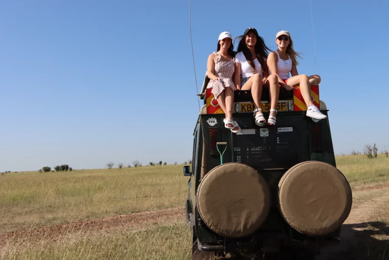 Group tour travel- three tourists pose for a pic seated on top of our safari landcruiser